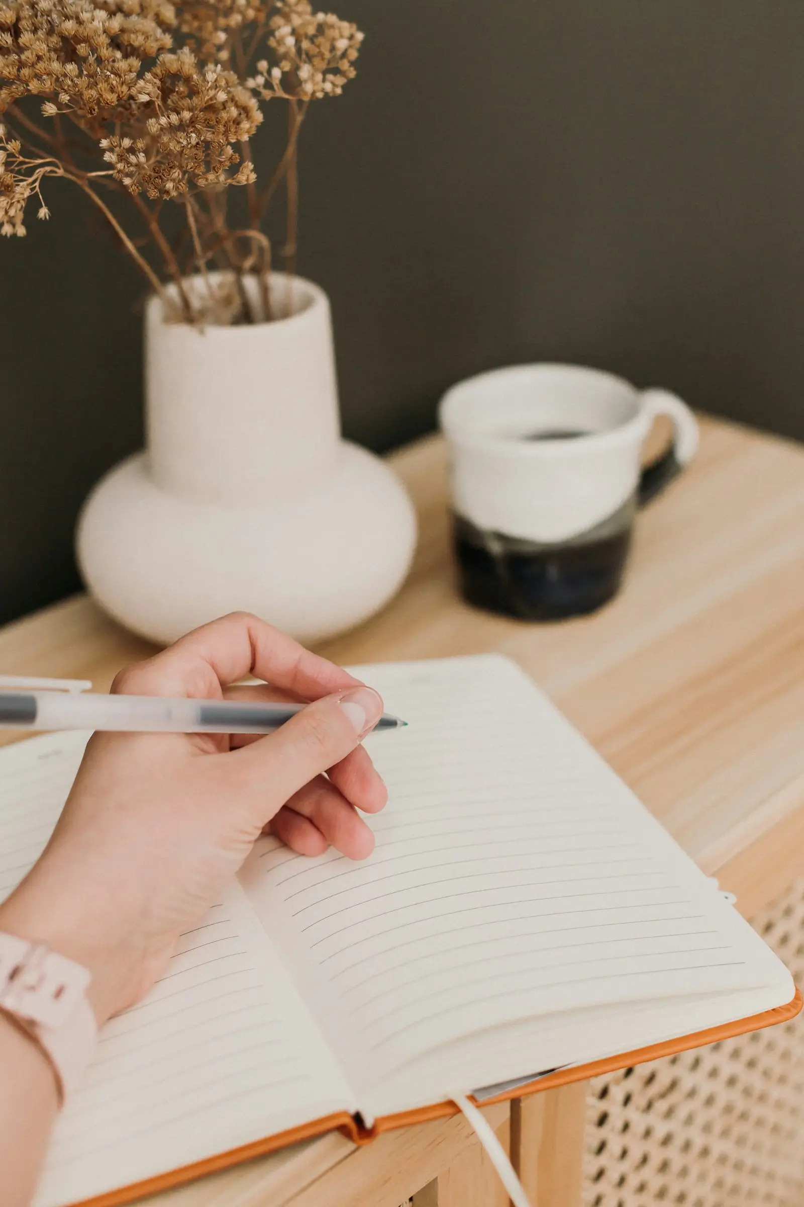 Une main écrit dans un carnet, sur un bureau en bois clair